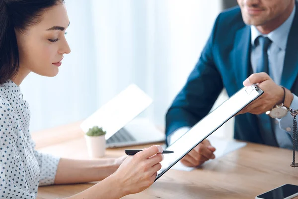 Cropped shot of lawyer holding clipboard and young woman signing document — Stock Photo