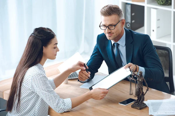 Smiling lawyer giving clipboard and pen to young woman in office — Stock Photo