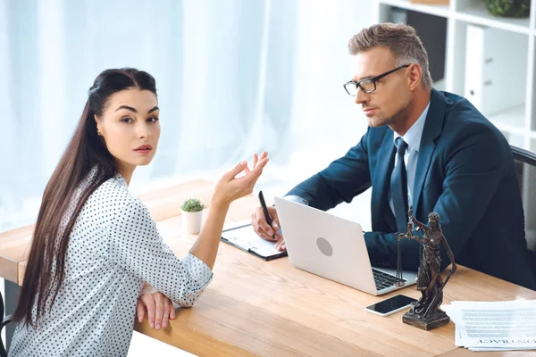 Anwalt macht sich Notizen und benutzt Laptop, während Klient in Kamera schaut — Stockfoto