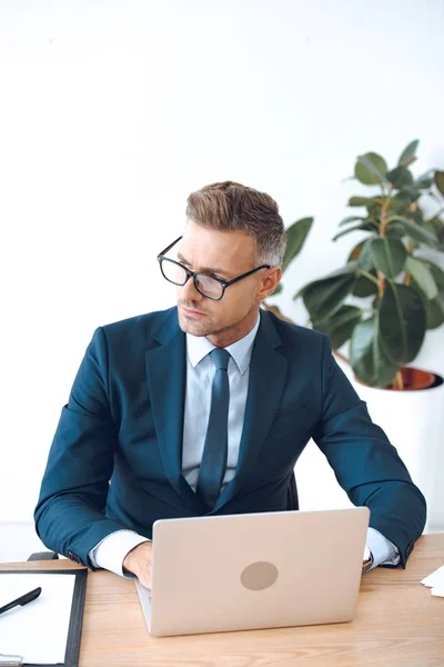 Vista de ángulo alto de guapo abogado en gafas usando el ordenador portátil y mirando hacia otro lado en la oficina - foto de stock