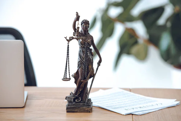 Vista de cerca de la estatua de la justicia dama, contrato y portátil en la mesa - foto de stock