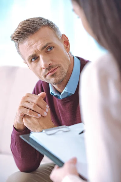 Cropped shot of adult patient looking at psychotherapist with clipboard — Stock Photo