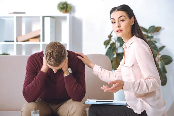 Psychotherapist looking at camera while supporting upset patient in office — Stock Photo