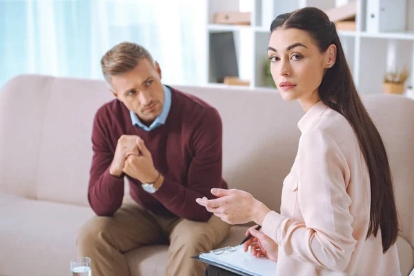 Psychologe macht Notizen und schaut in die Kamera, während er mit dem Patienten arbeitet — Stockfoto