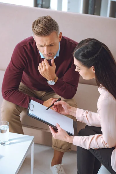 Female psychologist pointing at blank clipboard during therapy appointment with male patient — Stock Photo