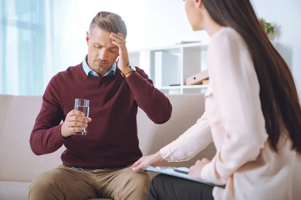 Patient masculin avec verre d'eau ayant rendez-vous de thérapie au bureau de psychologue — Photo de stock