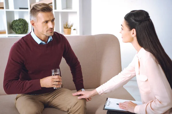 Patient masculin avec verre d'eau ayant rendez-vous de thérapie au bureau de psychologue — Photo de stock