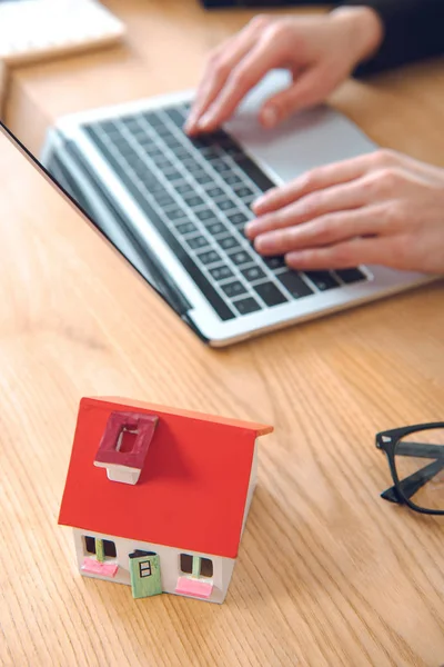 Cropped shot of businesswoman working on laptop at workplace with house model, house insurance concept — Stock Photo