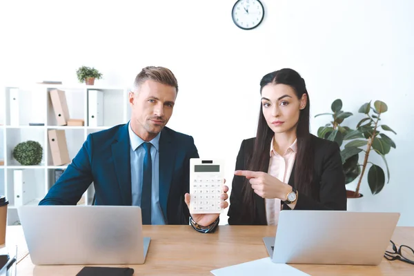 Porträt einer Geschäftsfrau, die am Arbeitsplatz im Büro auf Taschenrechner in der Hand von Kollegen zeigt — Stockfoto