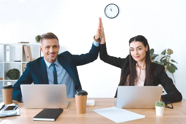 Portrait of business colleagues giving high five to each other at workplace with laptop in office — Stock Photo