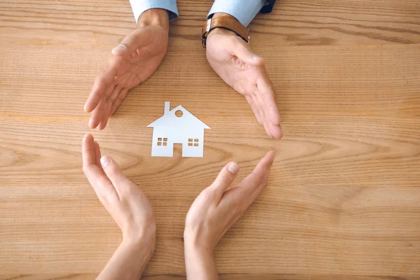 Partial view of insurance agents and female hands with paper house model on wooden tabletop, house insurance concept — Stock Photo