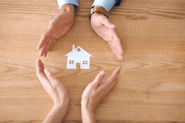 Vista parziale di agenti assicurativi e mani femminili con modello di casa di carta su tavolo in legno, concetto di assicurazione casa — Foto stock