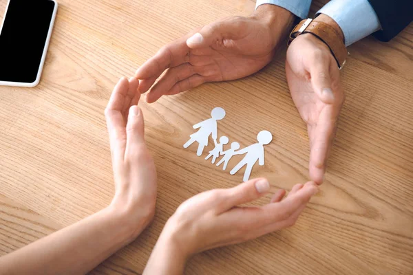 Partial view of insurance agents and female hands with family paper model on wooden tabletop, family insurance concept — Stock Photo