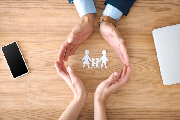 Partial view of insurance agents and female hands with family paper model on wooden tabletop, family insurance concept — Stock Photo