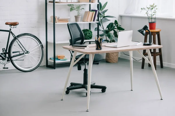 Interior de la moderna oficina de negocios con mesa, ordenador portátil y bicicleta - foto de stock