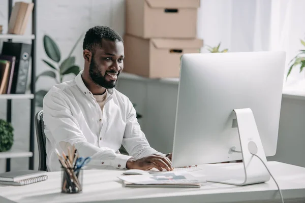 Lächelnd gut aussehender afrikanisch-amerikanischer Geschäftsmann im weißen Hemd, der im Büro am Computer arbeitet — Stockfoto