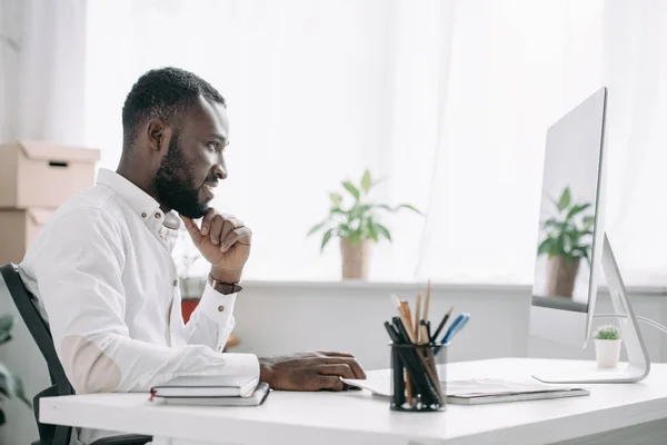 Vue de côté de joyeux beau homme d'affaires afro-américain travaillant à l'ordinateur dans le bureau — Photo de stock