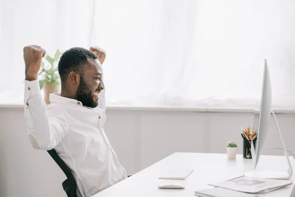 Side view of happy african american businessman working at computer in office and showing yes gesture — Stock Photo