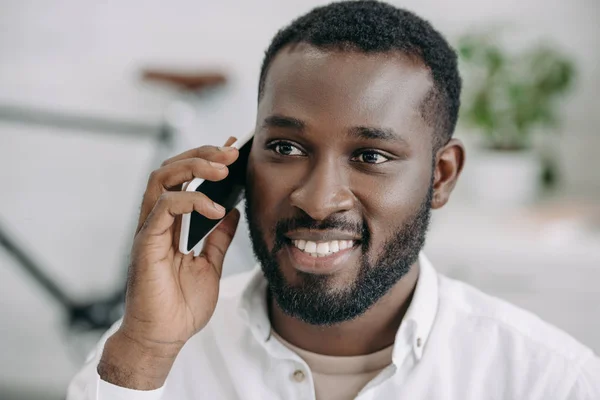 Retrato de sonriente guapo afroamericano hombre de negocios hablando por teléfono inteligente en la oficina - foto de stock