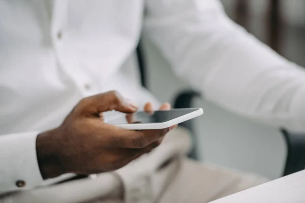 Imagem recortada do empresário afro-americano usando smartphone no escritório — Fotografia de Stock