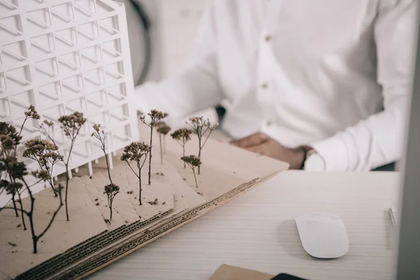 Imagen recortada del arquitecto afroamericano sentado cerca del modelo de arquitectura en la mesa en la oficina - foto de stock