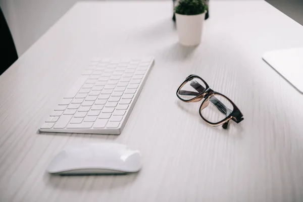 Tastiera del computer, mouse del computer e occhiali su un tavolo bianco in ufficio — Foto stock