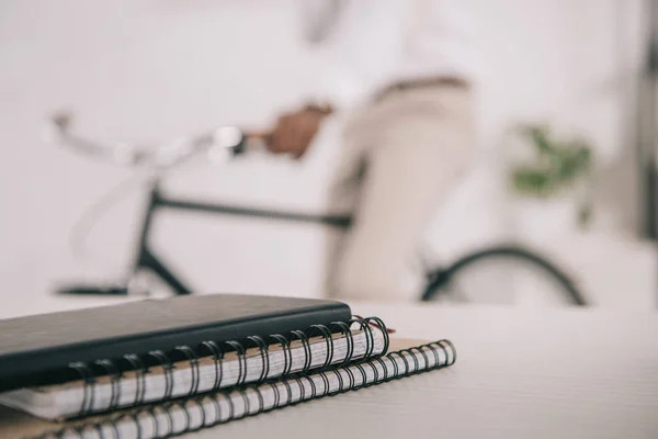 Imagem recortada do empresário afro-americano sentado de bicicleta no escritório, cadernos em mesa em primeiro plano — Fotografia de Stock