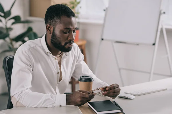 Schöner afrikanisch-amerikanischer Geschäftsmann sitzt am Tisch und schaut im Büro auf die Brille — Stockfoto