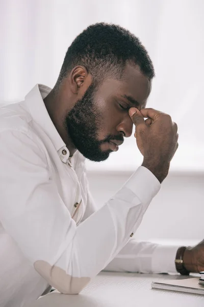 Vue latérale d'un homme d'affaires afro-américain fatigué touchant le pont du nez au bureau — Photo de stock