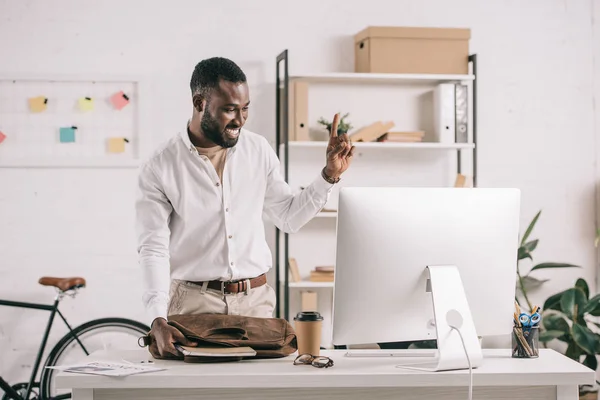 Alegre guapo africano americano hombre de negocios apuntando hacia arriba en la oficina y mirando la computadora - foto de stock