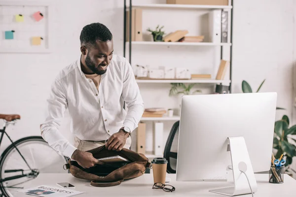 Beau souriant homme d'affaires afro-américain mettre des carnets dans la mallette dans le bureau — Photo de stock