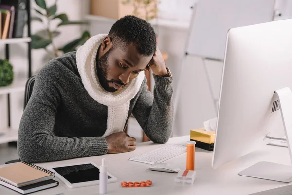 Hombre afroamericano enfermo sentado en el lugar de trabajo con computadora y tratamiento - foto de stock