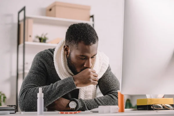 Bearded ill african american businessman coughing at workplace with medicines — Stock Photo