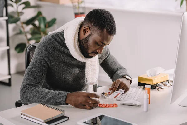 Засмучений хворий афро-американських бізнесмен з таблетки і склянку води, сидячи на робочому місці в офісі — стокове фото