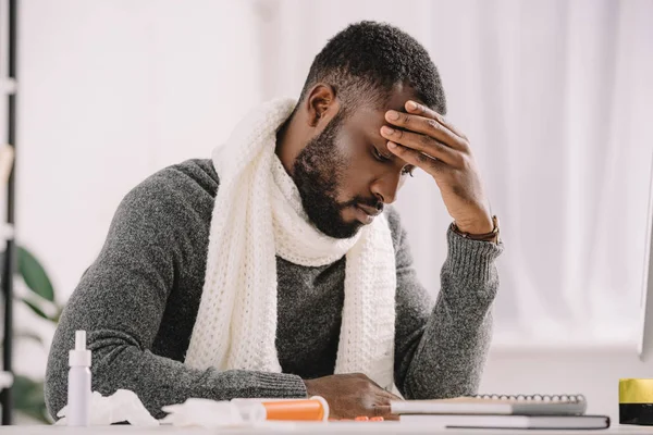 Tired african american man sitting at workplace with medicines in modern office — Stock Photo