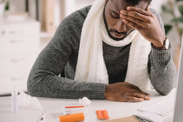 Cansado afro-americano com dor de cabeça olhando para pílulas enquanto sentado no escritório — Fotografia de Stock