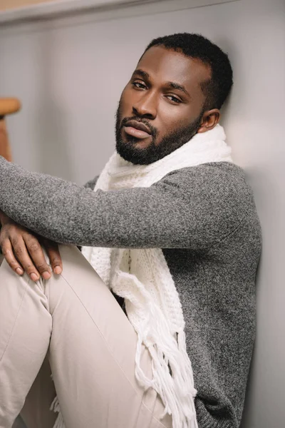 Больной афроамериканец в теплом шарфе сидит на полу — стоковое фото
