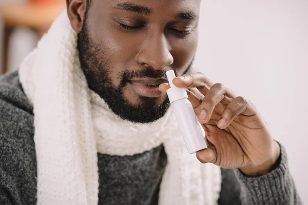 Ill african american man in warm scarf with nose spray — Stock Photo