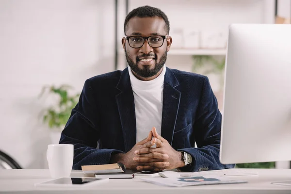 Hombre de negocios afroamericano sonriente elegante que trabaja con la computadora en oficina - foto de stock