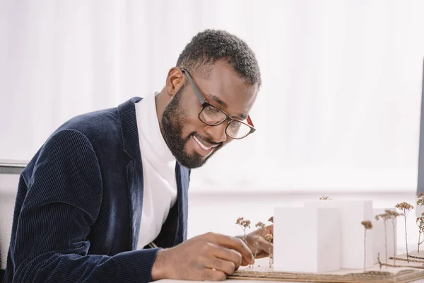 Sorridente barbudo afro-americano engenheiro trabalhando com modelo de edifícios de negócios — Fotografia de Stock