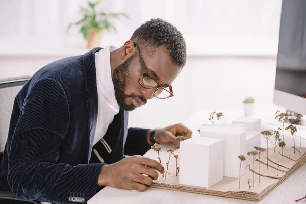 Arquitecto afroamericano concentrado profesional que trabaja con el modelo de edificios de negocios - foto de stock