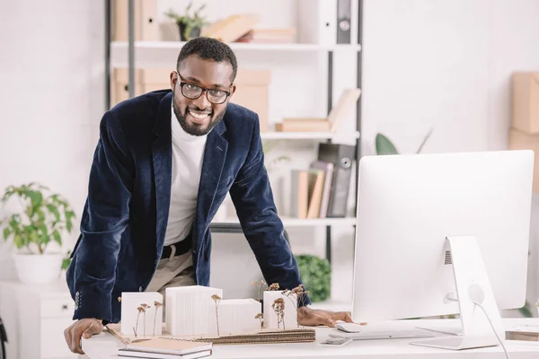 Erfolgreicher afrikanisch-amerikanischer Architekt arbeitet mit Geschäftsgebäudemodell und Computer im modernen Büro — Stockfoto