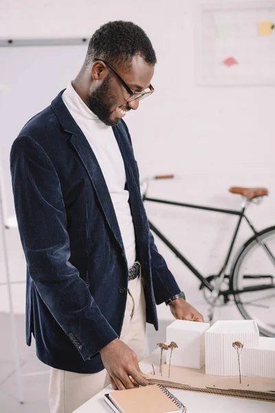 Professional cheerful african american architect working with business buildings model in office — Stock Photo