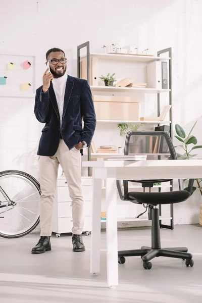 Empresário afro-americano alegre falando no smartphone no escritório moderno — Fotografia de Stock