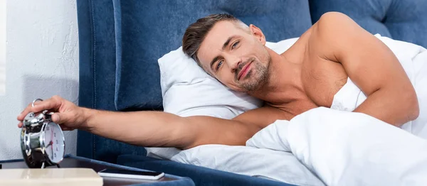 Красивый взрослый мужчина выключает будильник в утреннее время дома — стоковое фото