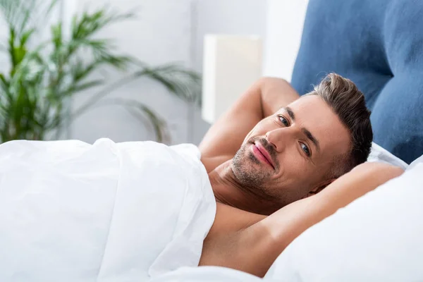 Selective focus of happy adult man laying in bed at home — Stock Photo