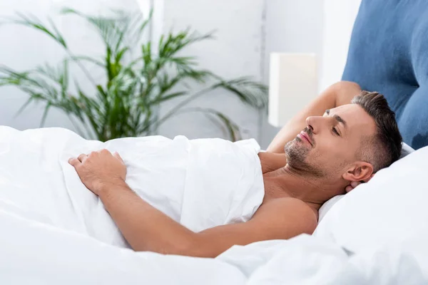 Vue latérale de l'homme adulte joyeux couché dans le lit à la maison — Photo de stock