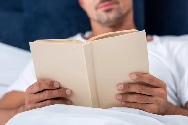 Abgeschnittenes Bild eines Mannes, der Buch liest, während er morgens zu Hause im Bett liegt — Stockfoto
