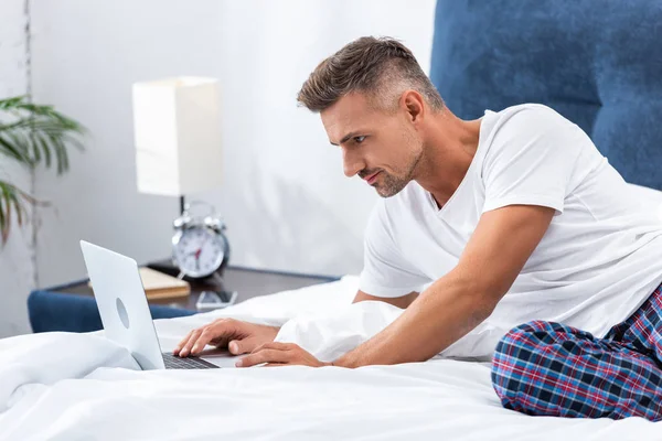 Adult male freelancer laying in bed and using laptop during morning time at home — Stock Photo