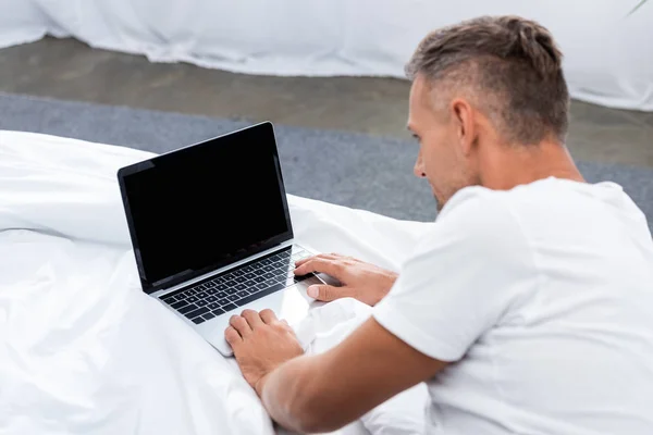 Rückansicht eines Mannes, der im Bett liegt und zu Hause Laptop mit leerem Bildschirm benutzt — Stockfoto